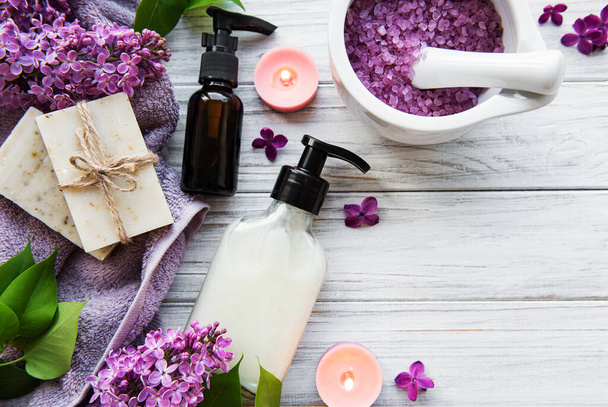 Spa setting with lilac flowers. Sea salt in bowl, bottles with aroma oil  and candles on wooden background.  - Φωτογραφία, εικόνα