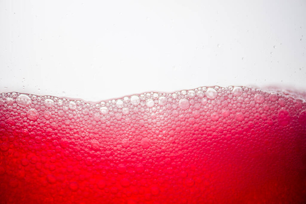 Fondo de burbujas de soda de primer plano mezclado con jugo de fruta roja sobre fondo blanco
. - Foto, Imagen
