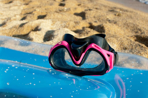 pink diving mask for girls on blue sea mattress on sunny day at the beach with sand as background, close up - Photo, Image