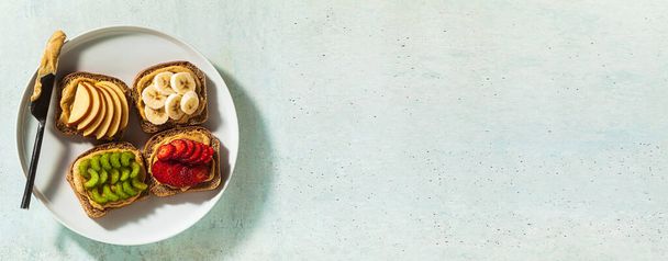 spandoek van diverse sandwiches met pindakaas en aardbeien, selderij, banaan en appel op een bord op tafel. perfecte ochtend ontbijt - Foto, afbeelding