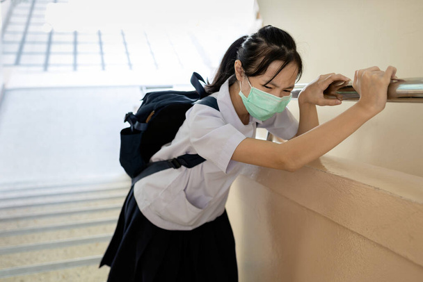 Estudante vestindo um uniforme escolar com uma máscara protetora, menina cansada tem dificuldade em respirar, doença, infectada com Coronavirus, doença de Covid-19 na escola durante sua reabertura, de volta à escola
 - Foto, Imagem