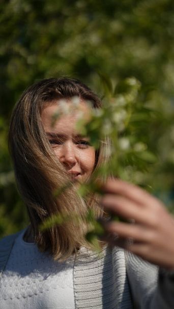 Ritratto di una donna attraente ed elegante con i capelli lunghi in un parco primaverile sullo sfondo di alberi in fiore. Maturo concetto di bellezza
 - Foto, immagini