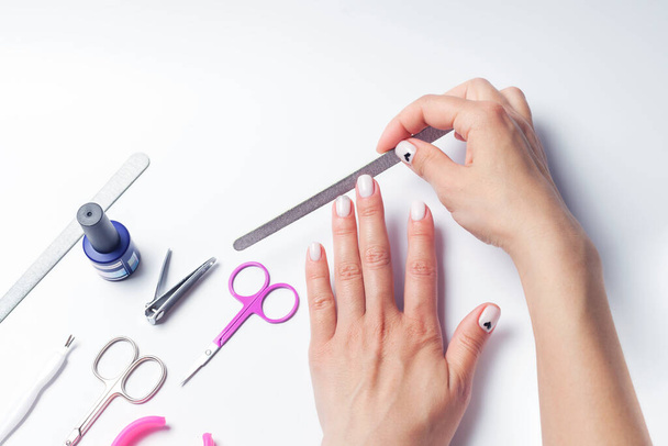 Female hands hold a nail file, next to lay down devices for nail care. The girl does a manicure. on white background. View from above. High quality photo - Foto, afbeelding