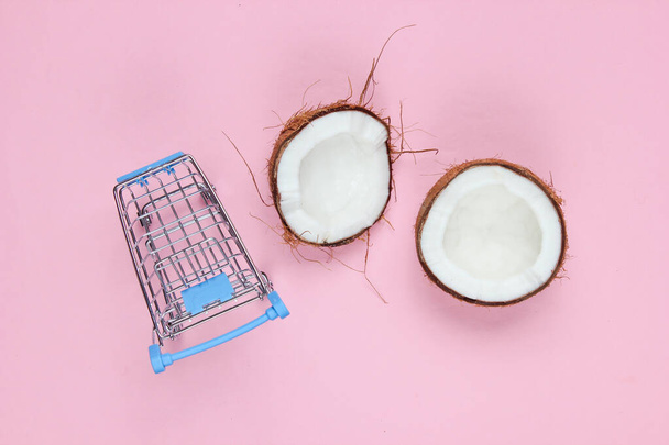 Concetto di shopping di frutta. Carrello della spesa, metà noce di cocco spezzata su fondo rosa. Vista dall'alto
 - Foto, immagini