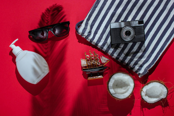 Creatieve reisachtergrond. Strand accessoires, retro camera, kokosnoot, schaduw van palmbladeren op rode achtergrond. Vlakke zomerse stijl. Bovenaanzicht - Foto, afbeelding