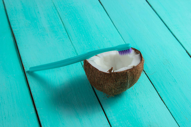 Koncept ekologických výrobků pro péči o zuby. Kartáček na zuby a půl kokosu na modrém dřevěném pozadí - Fotografie, Obrázek