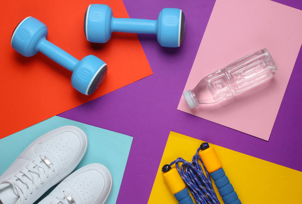 Flat lay style sport concept. Dumbbells, sneakers, jump rope, bottle of water. Sports equipment on colored background. Copy space. Top view - Foto, imagen