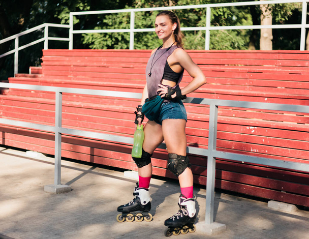 Iloinen nainen urheiluvaatteissa ja rullaluistimet poseeraa skate park. Ulkoilun käsite. Harrastus. Urheiluelämäntapa - Valokuva, kuva