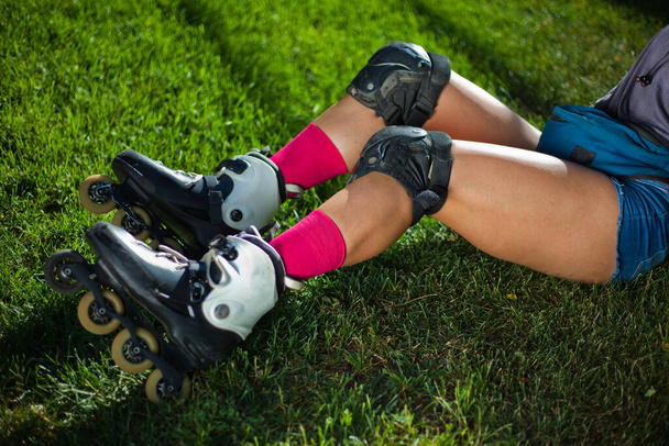 Young woman in protective gear and roller skates is sitting in the park on the grass. The concept of outdoor activities. Hobby. Sport lifestyle - Photo, Image