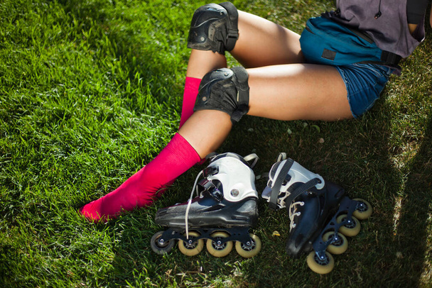Female legs in pink long socks and roller skates are sitting on the grass lawn. - Zdjęcie, obraz