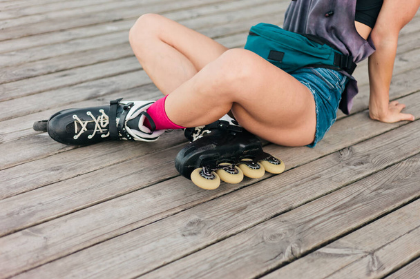 Vrouwenrolschaatser zit buiten houten planken. Foto benen bijsnijden. Sport levensstijl - Foto, afbeelding