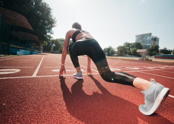 Žena běžkyně ve sportovním oblečení se chystá běžet sprint na nízkém startu venkovní. Zadní pohled - Fotografie, Obrázek
