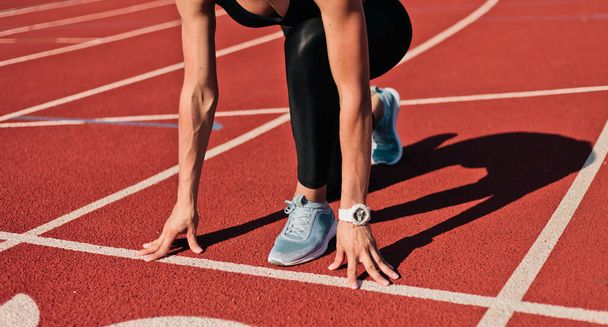 Mladá běžkyně ve sportovním oblečení se chystá běžet sprint na nízkém startu na stadionu trati s červenou potaženou za jasného slunečného dne. Oříznout fotografii - Fotografie, Obrázek