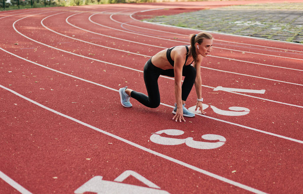 Spor giyimli genç bir bayan kırmızı kaplamalı stadyum pistinde kısa mesafe koşusuna hazırlanıyor.  - Fotoğraf, Görsel