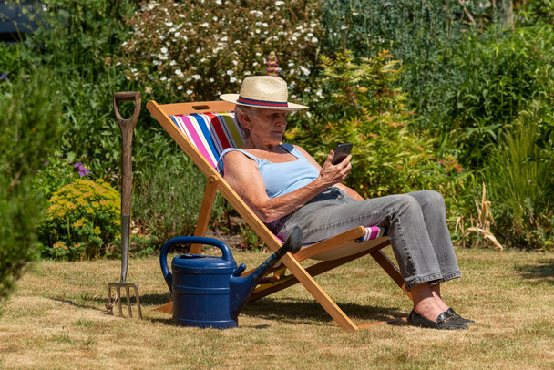 Hampshire, İngiltere, İngiltere. 2020 yılı. Sıcak bir yaz gününde terasta oturarak bahçeye ara veren bir kadın.. - Fotoğraf, Görsel