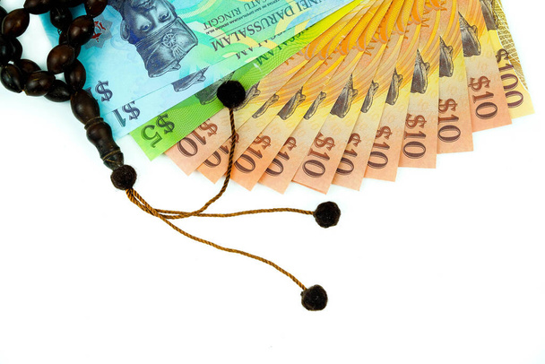 Μουσουλμανικές χάντρες προσευχής και κοντινό πλάνο πολύχρωμων χαρτονομισμάτων του brunei σε διάφορες αξίες των $1, $5, $10, $100 πάνω από το λευκό. Επικέντρωση στα τραπεζογραμμάτια. - Φωτογραφία, εικόνα