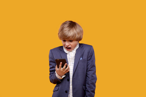 Um menino loiro assustado com um rosto assustado olha para o telefone
. - Foto, Imagem
