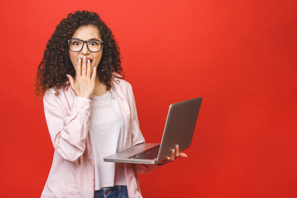 Ritratto di donna sorpresa felice scioccata in piedi con computer portatile isolato su sfondo rosso
. - Foto, immagini
