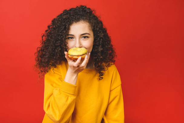 Close up portrait of a satisfied pretty young girl eating donuts isolated over red background. - Fotografie, Obrázek