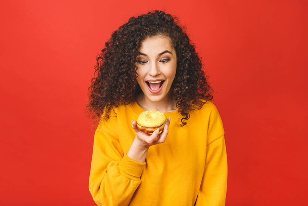 Close up portrait of a satisfied pretty young girl eating donuts isolated over red background. - Fotó, kép