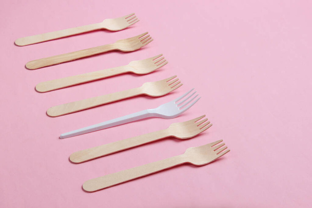 Concepto ambiental minimalista. Tenedores de madera y plástico sobre fondo pastel rosado. Fondo ecológico creativo
 - Foto, imagen
