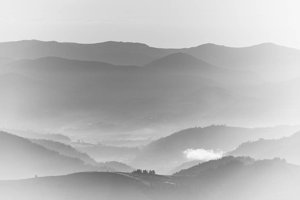 Вид на вершину при фантастическом солнечном свете красивых живописных гор на восходе. Слои горы и туман в холмах на расстоянии. Черно-белый пейзаж. Высокий фон для фотографии ключа
. - Фото, изображение