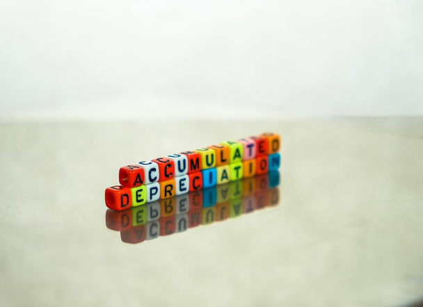 Colorful alphabet beads stacked forming the words over reflective table. Conceptual of accumulated depreciation in financial statements.  Focus on text on beads at front. - Photo, Image