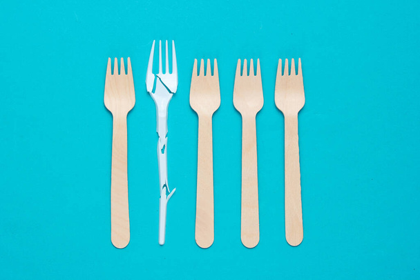 Minimalistic ecologically clean still life. Pop Art. Broken plastic fork among many wooden forks on blue background. Cutlery made from natural materials - 写真・画像