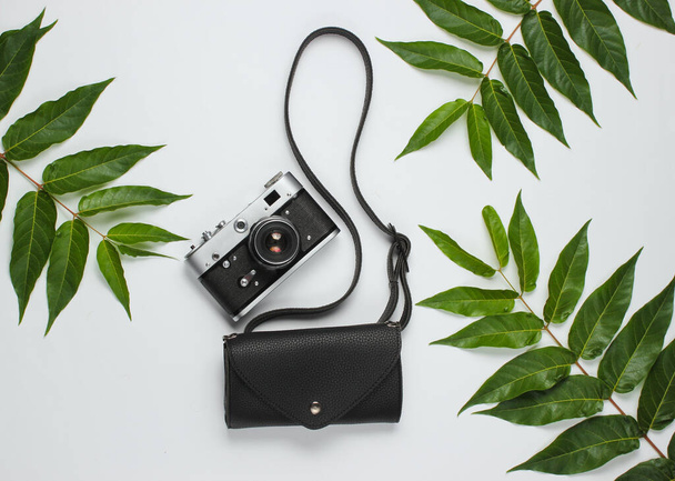 Leather waist bag, retro camera on white background with green tropical leaves. Top view - Photo, Image
