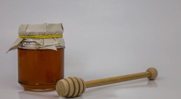 Скляна банка з медом і дерев'яна паличка на білому тлі
 - Фото, зображення