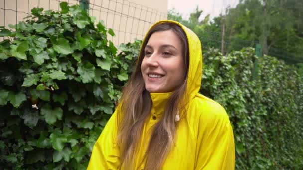 Fröhliche junge Frau in gelbem Regenmantel genießt den Sommerregen im Freien. Mädchen lächelt und hebt im Nieselregen glücklich die Arme - Filmmaterial, Video
