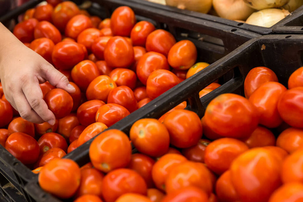 Ψώνια. Γυναίκα που επιλέγει το βιολογικό φρούτο τομάτας σε κατάστημα λαχανικών ή supermarket.Μια γυναίκα χέρι που κατέχουν κόκκινες ντομάτες, επιλέξτε μεταξύ φρέσκα και μαραμένα. Επιλογή στιγμιότυπου. - Φωτογραφία, εικόνα