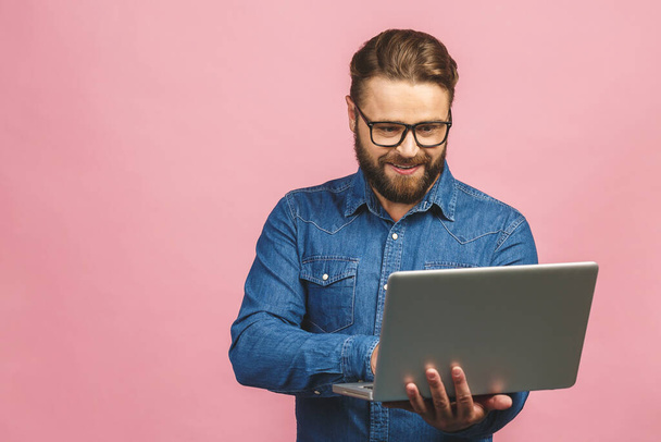 Zelfverzekerde zakenexpert. Zelfverzekerde jonge knappe man in casual holding laptop en glimlachen terwijl staan tegen geïsoleerde roze achtergrond. - Foto, afbeelding