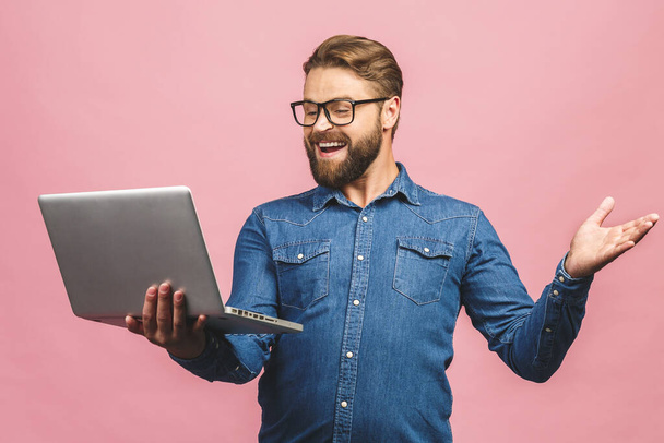 Selbstbewusster Wirtschaftsexperte. Selbstbewusster junger gutaussehender Mann im Hemd, Laptop in der Hand und lächelnd vor rosa Hintergrund stehend. - Foto, Bild