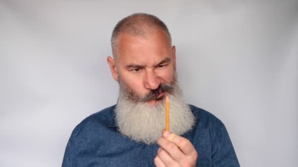 Mature man sharpens pencil with planer. Funny bearded grandfather grimaces funny. Portrait of senior man on gray background. - Footage, Video