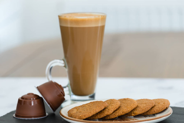 Tall glass of Latte and some coffee and Ginger biscuits on a plate with some cream pods also. . - Fotó, kép