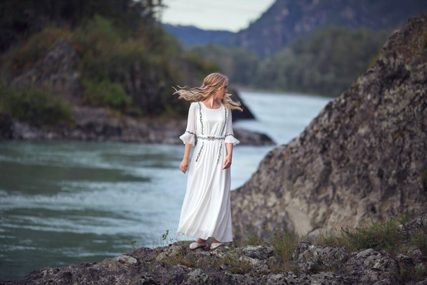 Conte de fées. L'histoire de la fée de la rivière. Tir dans l'Altaï. Une fille en robe blanche marche sur un rivage rocheux près de la rivière
. - Photo, image