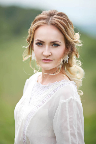 de bruid wandelt in het veld tegen de achtergrond van de bergen, een fotoshoot in Altai, een portret van de bruid, een meisje in een witte jurk in de stijl van boho - Foto, afbeelding