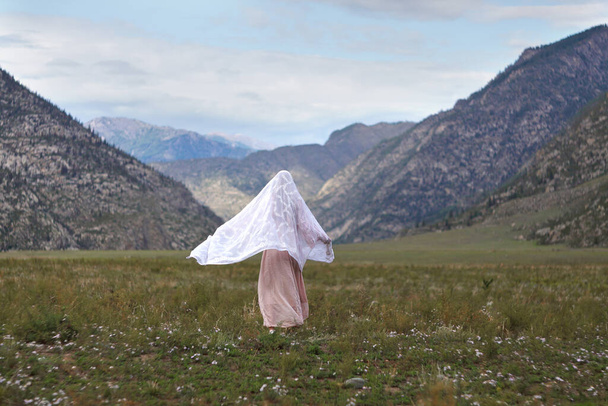 Παραμύθι. Ένα κορίτσι με ευγενικό τρόπο περπατά μέσα από το λιβάδι με φόντο τα βουνά. Συνομιλία με τον Θεό. Προσευχή. - Φωτογραφία, εικόνα