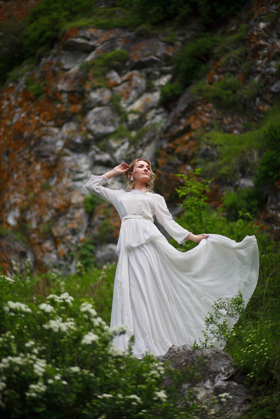 die Braut geht auf dem Feld vor der Kulisse der Berge, ein Fotoshooting im Altai, ein Porträt der Braut, ein Mädchen in einem weißen Kleid im Boho-Stil - Foto, Bild