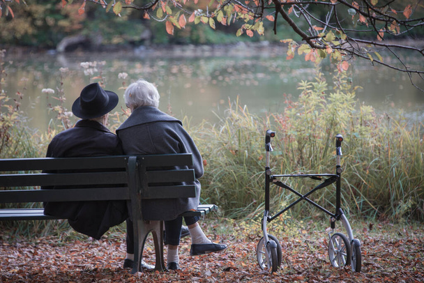 Pareja mayor hombre y mujer están descansando en un banco en el parque de otoño. Efecto imágenes en color neutro y pastel
. - Foto, imagen