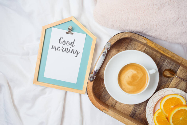 Coffee cup and fresh oranges on wooden tray on morning bed background. Top view from above - Foto, imagen