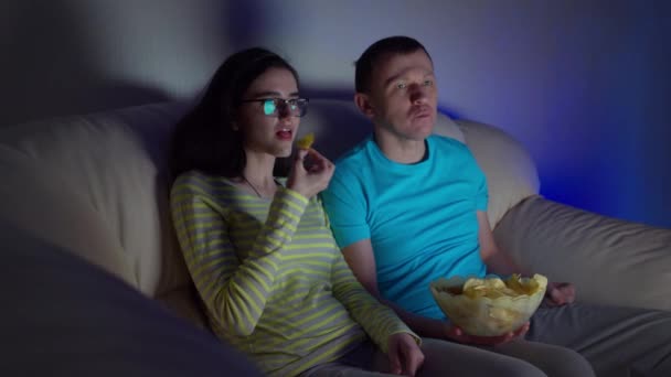 夜遅くまで若いですカップル見ますAムービーでテレビと食べるチップながら、ソファに座って - 映像、動画
