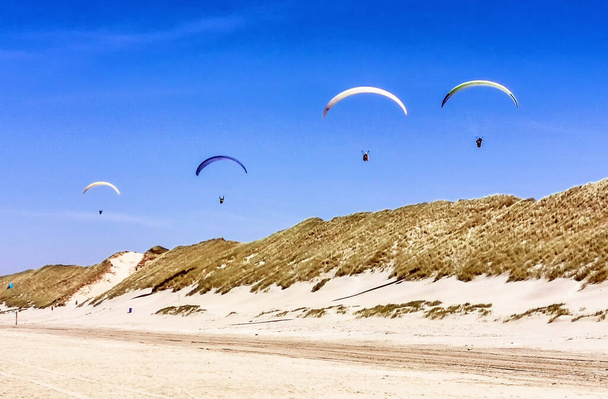 Parapente volando por encima de las dunas en la playa divirtiéndose y una gran aventura
. - Foto, imagen
