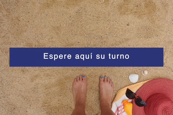 ビーチで砂と足を持つ背景,夏に社会的距離の概念,スペイン語でテキスト:ここであなたの順番を待ちます. - 写真・画像