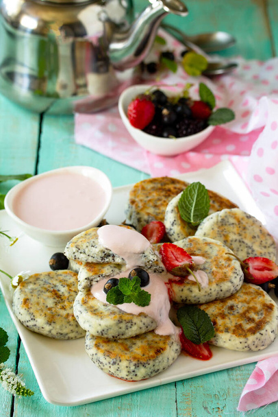 Zomer ontbijt. Huisgemaakte kwark pannenkoeken met maanzaad, zure roomsaus met aardbeien.  - Foto, afbeelding
