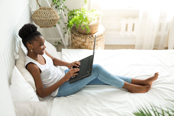 beautiful young african woman sitting on bed with laptop - Foto, imagen