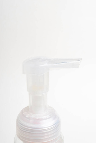 Una imagen de cerca de la bomba superior translúcida de un dispensador de botellas de plástico de jabón de espuma sobre un fondo blanco
. - Foto, Imagen
