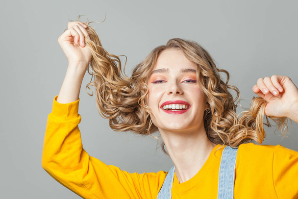 Красивая молодая женщина с длинными вьющимися волосами смеется на сером фоне
 - Фото, изображение
