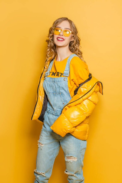 幸せなファッションモデル女性で冬のジャケットで明るい黄色の背景 - 写真・画像